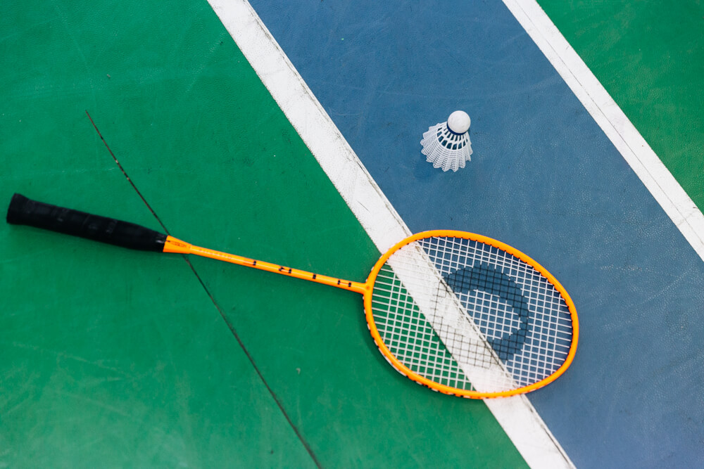 Federball und Badmintonschläger liegen auf grün-blau-weißem Boden.