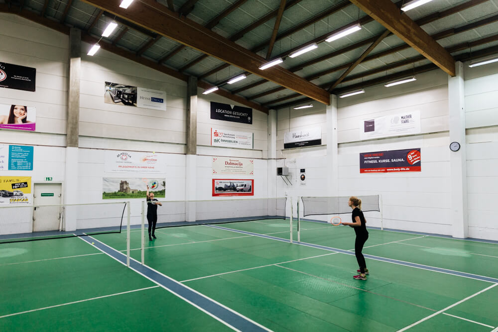 Zwei Frauen spielen Badminton auf einem von drei Badminton-Feldern.
