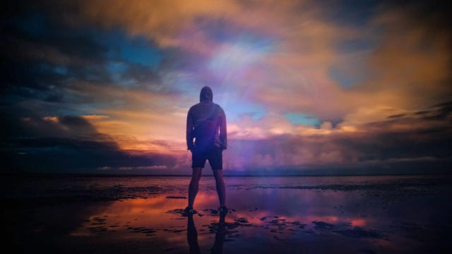a man is standing triumphant on a beach and watches the sunset