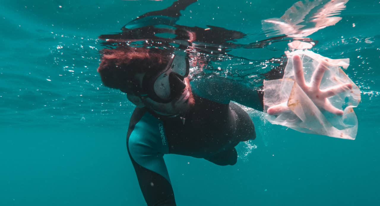 Man fishes a plastic bag from the ocean while diving