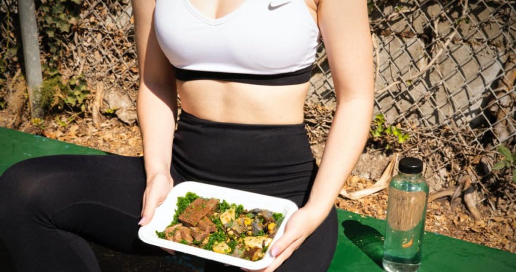 women is eating an high protein steak + veggies dish after-workout.
