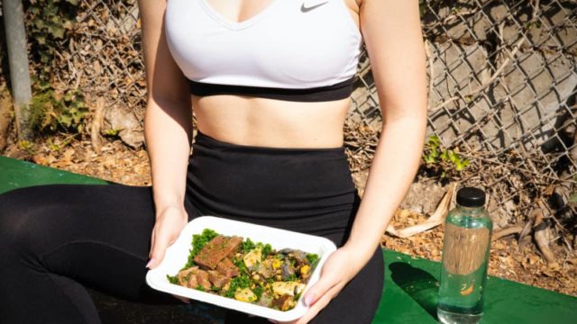 women is eating an high protein steak + veggies dish after-workout.