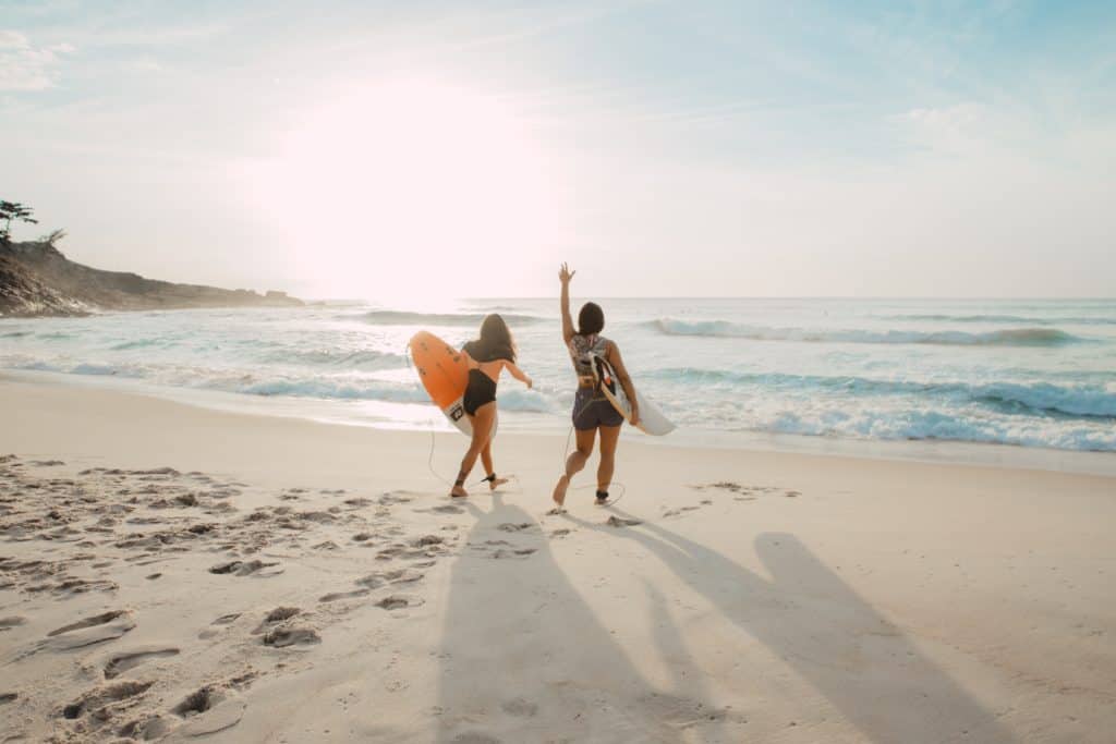 duas mulheres na praia com pranchas de surf dirigem-se para a água